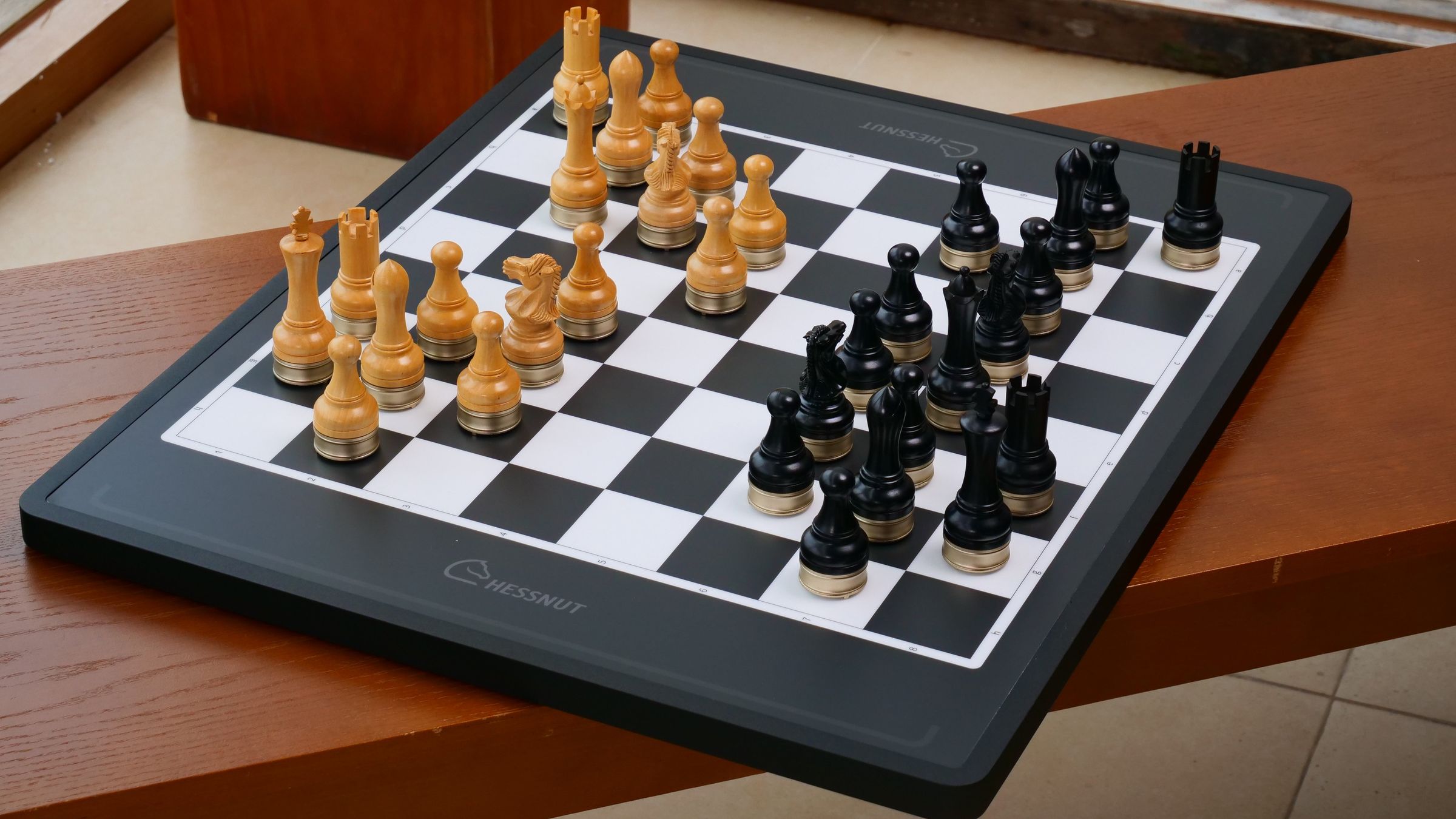 Chessnut Move с деревянными фигурами на деревянном столе у окна
