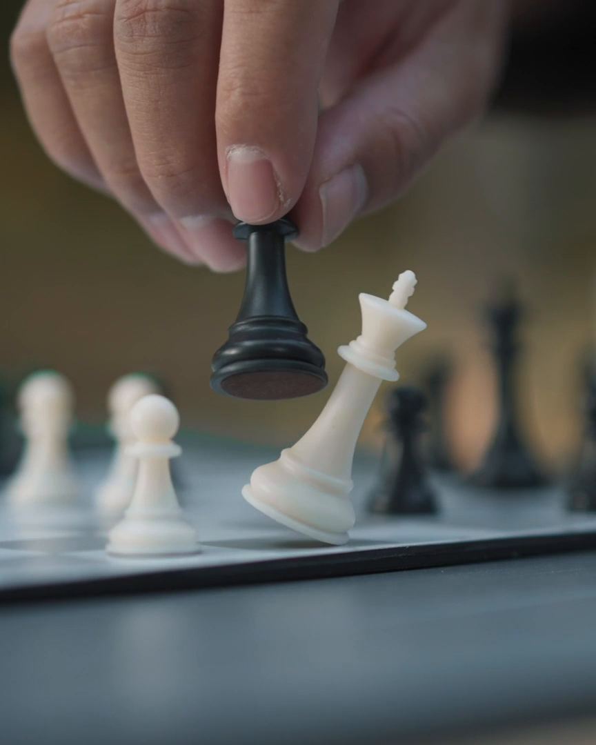 Рука чёрной фигурой роняет белого короля на доске Chessnut Go